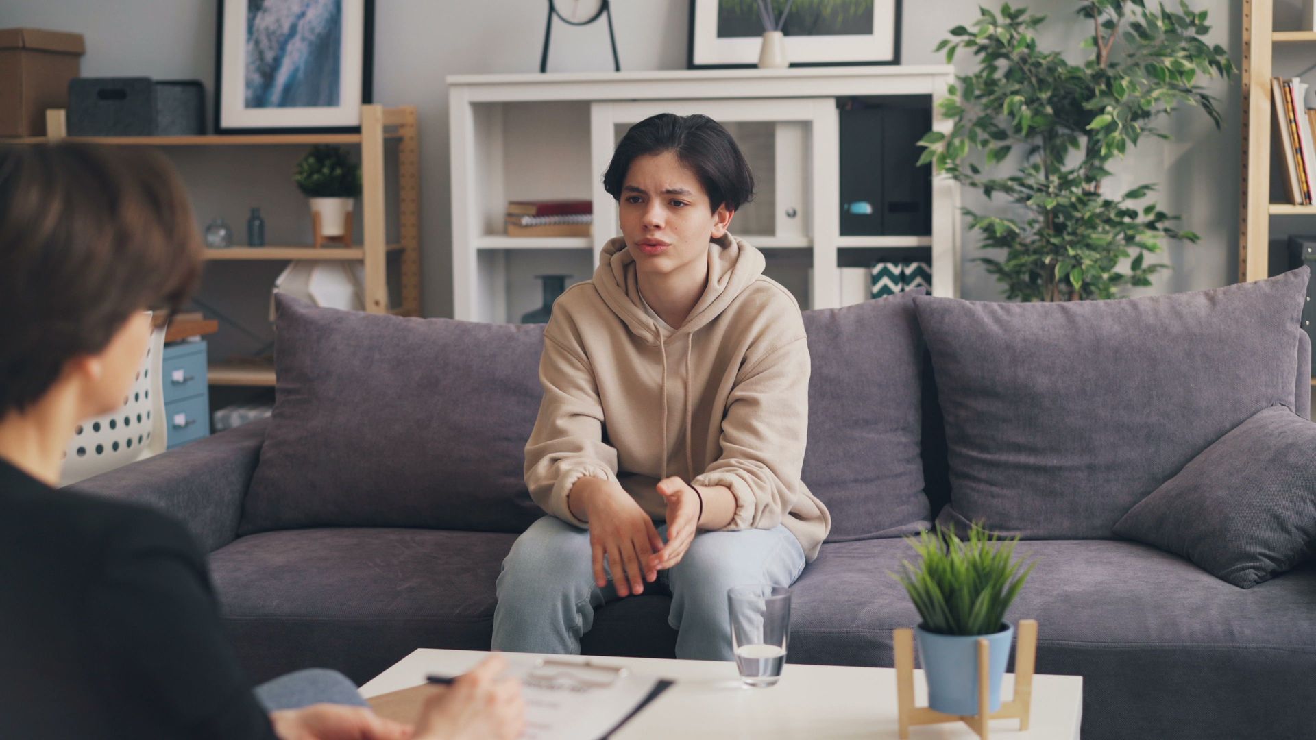 Teenager attending therapy session in a modern office, expressing emotions.