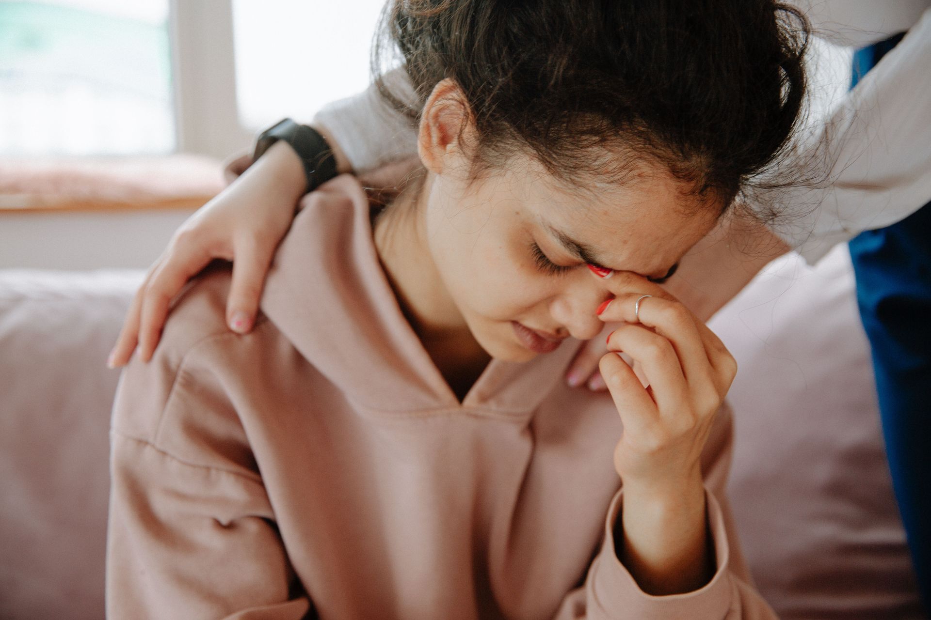 A young woman experiences emotional support from a friend in a comforting embrace.